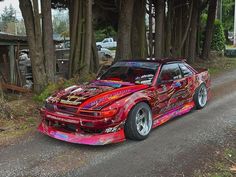 a colorful car parked on the side of a road next to some trees and bushes