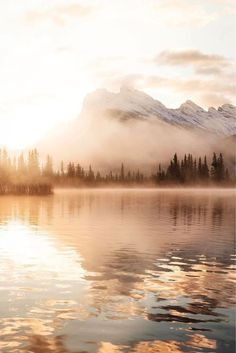 the sun is setting over a lake with mountains in the background and fog on the water