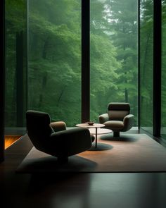 a living room with two chairs and a table in front of large glass windows that look out onto the woods