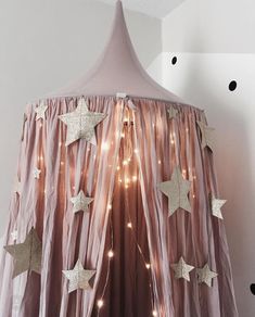 a pink canopy with white stars hanging from it's sides and lights on the ceiling