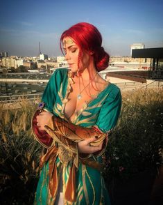 a woman with red hair wearing a green and gold dress standing on top of a roof