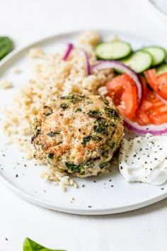 a white plate topped with meat, rice and veggies next to cucumbers