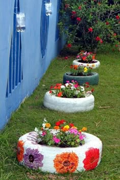 flower pots made from old tires are lined up on the grass in front of a blue wall