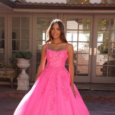 a woman in a pink ball gown standing on a patio with her hands behind her back