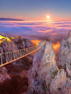 there is a bridge above the clouds on top of a mountain at night with a full moon in the sky