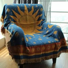 a chair covered in a blue and yellow blanket with sun design on the back, sitting next to a window