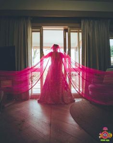 a woman standing in front of a window wearing a long pink dress with sheer sleeves