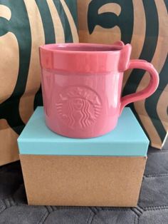 a pink starbucks cup sitting on top of a blue box next to some decorative pillows