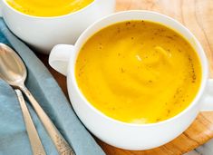 two white bowls filled with soup on top of a wooden cutting board next to silverware