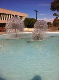 two water spouts in the middle of a pool with trees and buildings behind them