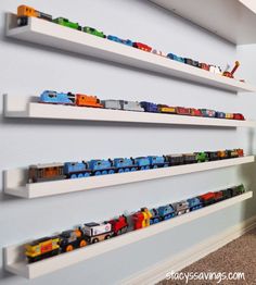 there are many toy trains on the shelves in this children's room that is painted white