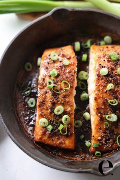 two salmon fillets in a skillet with green onions