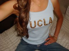 a beautiful young woman sitting on top of a bed wearing jeans and a tank top