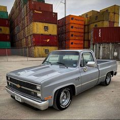 a silver truck parked in front of stacks of shipping containers