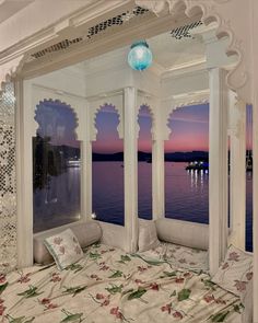 a bed sitting next to a window covered in white curtains and pillows on top of a bed