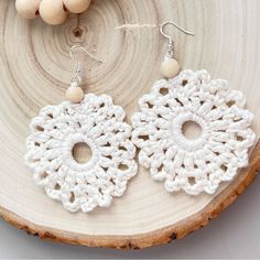 a pair of crocheted white earrings sitting on top of a piece of wood