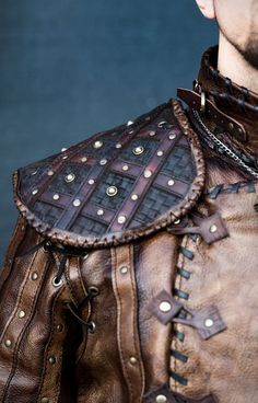 a close up of a man wearing a leather jacket with chains on his shoulders and shoulder