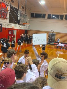 a group of people standing on top of a basketball court holding up signs that read meow