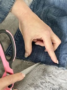 a person cutting fabric with scissors on top of the pair of jeans that they are holding