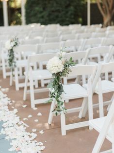 the aisle is lined with white chairs and flowers