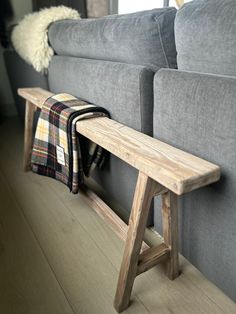 a wooden bench sitting in front of a gray couch next to a white and black plaid blanket