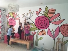 three children are standing on a bench in front of a painted wall with pink flowers