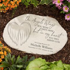 a memorial stone with an angel wings on it surrounded by flowers and plants in the background