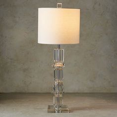 a glass table lamp with a white shade on the base and a marble wall behind it