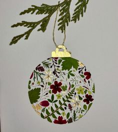 a christmas ornament hanging from a tree branch with leaves and flowers on it