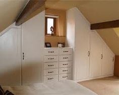 an attic bedroom with white furniture and drawers