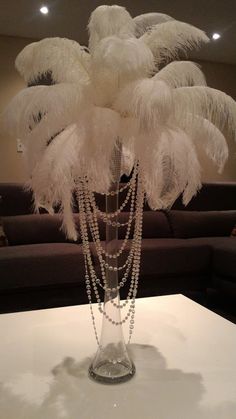 a glass vase filled with white feathers on top of a table next to a couch