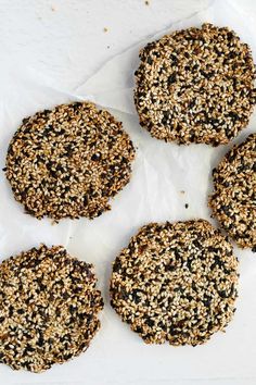 four cookies with seeds on them sitting on top of a piece of parchmented paper