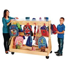 a woman standing next to a young boy in front of a school supply cart filled with backpacks