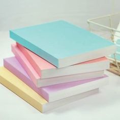 four different colored notebooks stacked on top of each other in front of a basket