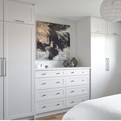 a bedroom with white cupboards and artwork on the wall above it's bed