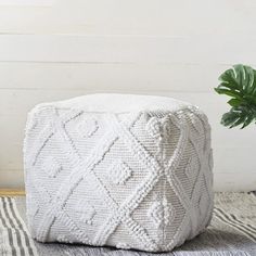 a white poufce sitting on top of a rug next to a potted plant