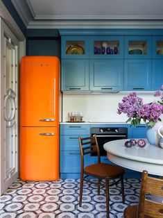 an orange refrigerator in a kitchen next to a table with chairs and flowers on it