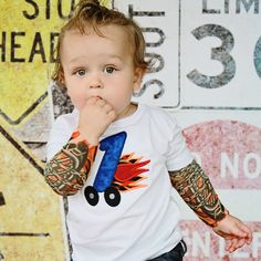 a little boy with tattoos on his arms and hands is standing in front of a gas station sign