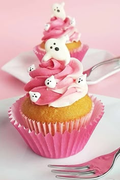 two cupcakes with pink frosting and ghost decorations