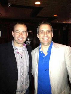 two men standing next to each other in a room with lights on and one man smiling at the camera