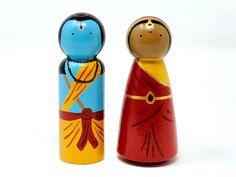 two wooden dolls are standing next to each other on a white surface, one is blue and the other is red