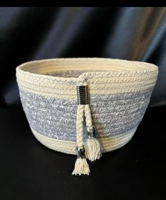 a white and gray basket with a black handle on a black tablecloth covered surface