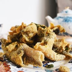 some fried food on a plate with a tea pot in the backgroung