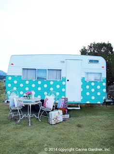 a blue and white trailer parked on top of a grass covered field next to a table with chairs