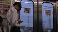 a man standing on a subway looking at his cell phone while holding onto the door