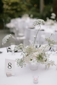 the table is set with white flowers and place cards for guests to sit down at