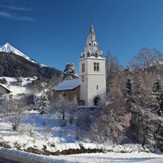 a church in the middle of winter with snow on the ground and mountains in the background