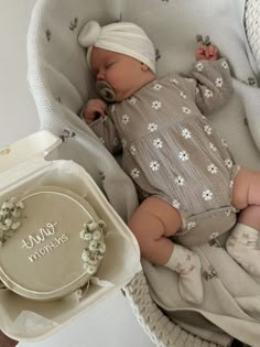 a baby is laying in a basket next to a plate and bowl with a name on it