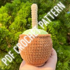 a hand holding a crochet potted plant in front of some green trees