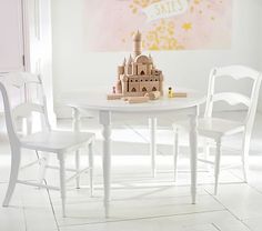 a white table with two chairs and a castle on it in front of a pink painting